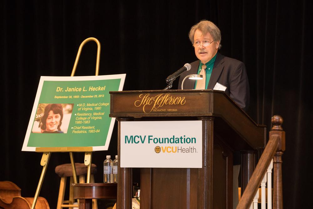Steven P. Heckel, speaks at the Endowed Scholarship Brunch next to a photo of his sister Dr. Janice Heckel, a 1980 alumna of the School of Medicine.