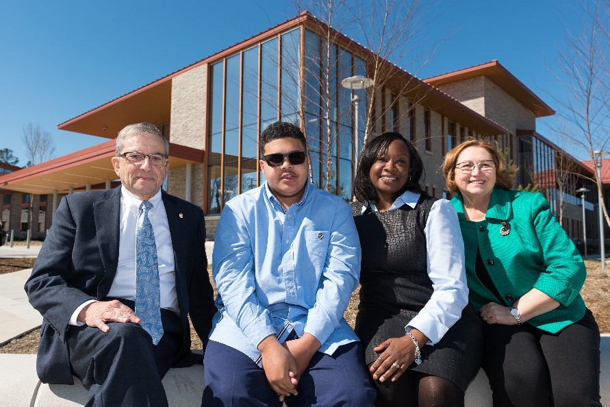 Joel Silverman, M.D., former chair of the VCU Department of Psychiatry (left) and Sandy Lewis, Ed.D., executive director of the Virginia Treatment Center for Children (right), sit with Kyle Gatewood and his mother Kiva outside the VTCC building on Richmond’s North Side. Kyle was treated by the VTCC at its original location starting at age 3, and Kiva delivered remarks at the new building’s ribbon cutting in 2017.