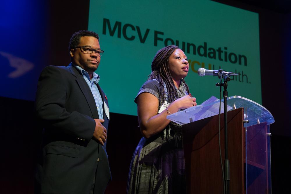 A woman gives a speech as a man listens at MCVF